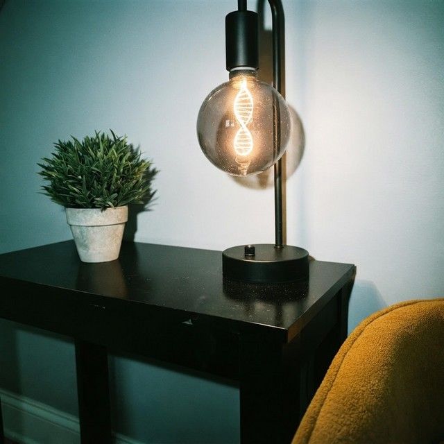 A bulb lamp glowing on a dark side table beside a small plant and a yellow chair